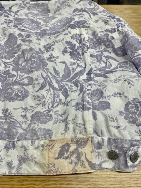 ローレンラルフローレンの白地に紫の花柄があしらわれたデニムジャケットの背面裾の革パッチからの色移りがキレイに落ちた染み抜きクリーニング事例（７，７００円税込、修理代も含む）2026.04.11