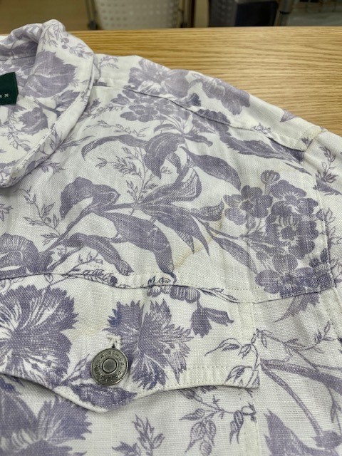 ローレンラルフローレンの白地に紫の花柄があしらわれたデニムジャケットの背面裾の革パッチからの色移りがキレイに落ちた染み抜きクリーニング事例（７，７００円税込、修理代も含む）2026.04.11